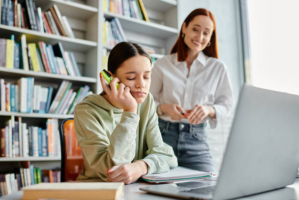 Skupiona ruda korepetytorka wielozadaniowa, ucząca nastolatkę rozmawiając przez telefon i korzystając z laptopa do lekcji pozalekcyjnych. - Zdjęcie, obraz