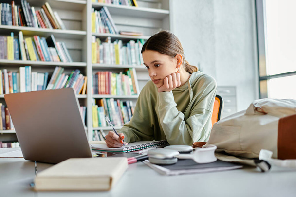 La adolescencia absorbe en el ordenador portátil mientras completa el trabajo escolar en un entorno de biblioteca sereno. - Foto, imagen