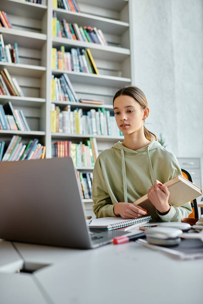 Ein Teenager vertieft in moderne Bildung, umgeben von Büchern und einem Laptop, der am Schreibtisch fleißig Hausaufgaben macht. - Foto, Bild