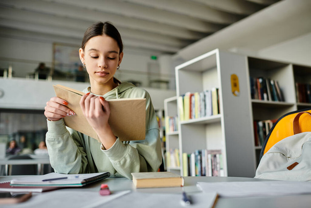 Egy tinédzser lány ül egy íróasztalnál, szorgalmasan ír egy jegyzetfüzetbe, az iskolai munkájára koncentrál órákon át tartó tanulás után.. - Fotó, kép