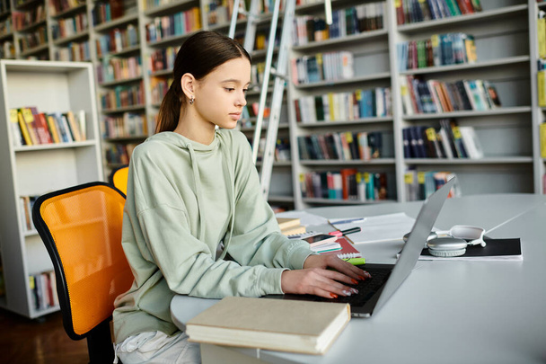 Ein Mädchen im Teenageralter lernt fleißig am Schreibtisch mit einem Laptop, umgeben von Regalen voller Bücher. - Foto, Bild