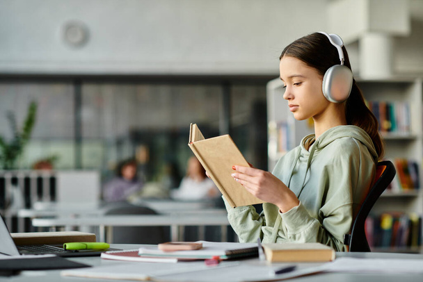 Ένα έφηβο κορίτσι βυθισμένο σε ένα βιβλίο βιβλιοθήκης φορώντας ακουστικά, βυθίζεται στα βασίλεια της λογοτεχνίας και της μουσικής.. - Φωτογραφία, εικόνα