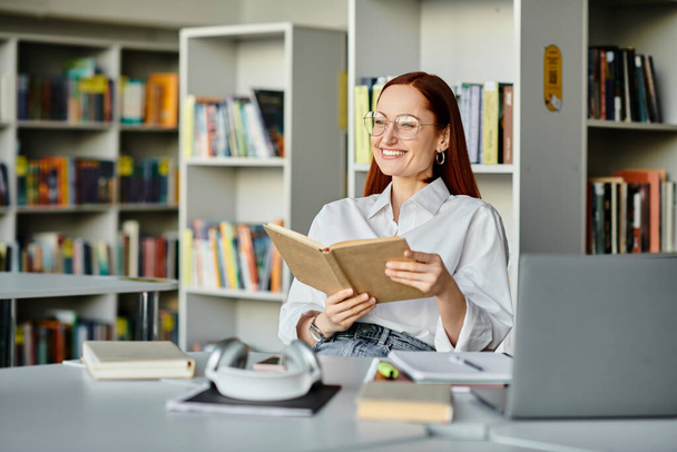 Una mujer pelirroja absorta en un libro, rodeada de estantes de libros en una biblioteca, absorbiendo el conocimiento. - Foto, imagen