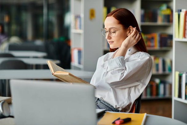 読書と学習に吸収された静かな図書館の設定で本に囲まれた赤毛の女性. - 写真・画像