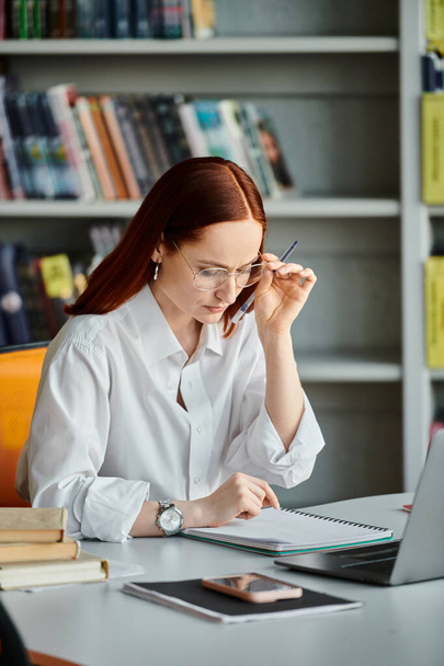 Uma tutor feminina ruiva está ensinando on-line usando um laptop em uma biblioteca depois de uma lição da escola. - Foto, Imagem