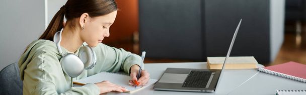 молодой студент делает домашнее задание с открытым ноутбуком, создавая инновационный образовательный контент. - Фото, изображение