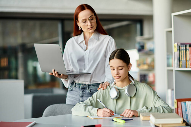 Une rousse donne des cours particuliers à une adolescente sur un bureau avec un ordinateur portable, qui suit des cours après l'école.. - Photo, image