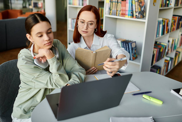 Opettaja, punapää nainen, opettaa teini-ikäistä tyttöä koulun jälkeen, käyttäen kannettavaa tietokonetta oppimisprosessin helpottamiseksi.. - Valokuva, kuva