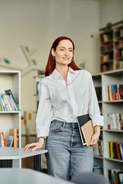 Redhead woman in a library, holding folder and smiling - Photo, Image