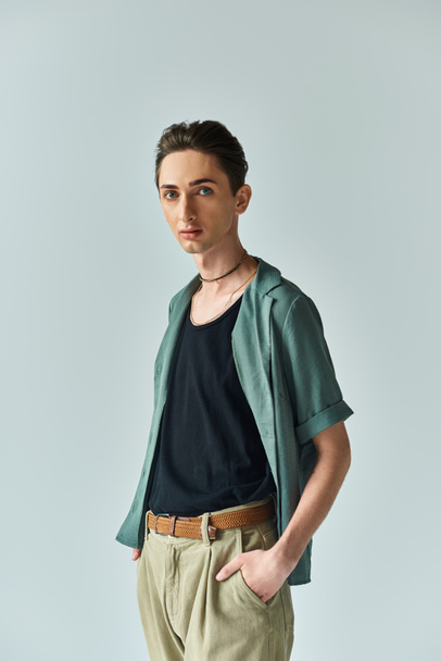 Ein junger Mann posiert stolz in grünem Hemd und brauner Hose und präsentiert seine lebendige queere Mode in einem Studio-Setting. - Foto, Bild