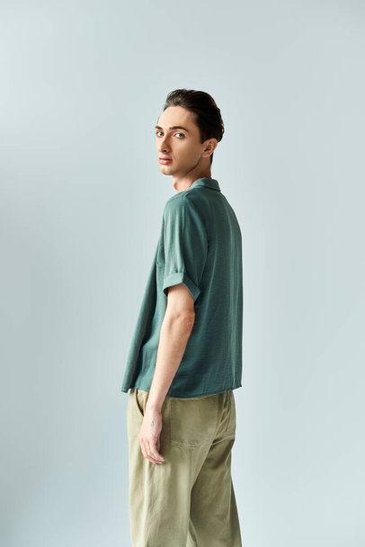Joven queer posa orgullosamente en una camisa de polo verde y pantalones caqui sobre un fondo gris del estudio. - Foto, imagen