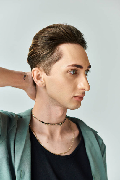 A young queer person proudly poses with a necklace around his neck in a studio setting, exuding confidence and pride. - Photo, Image