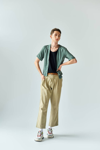 Young queer person confidently posing in studio wearing a tan shirt and khaki pants on a grey background. - Photo, Image
