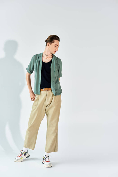 A young queer person in a tan shirt and khaki pants striking a pose in front of a white wall. - Photo, Image