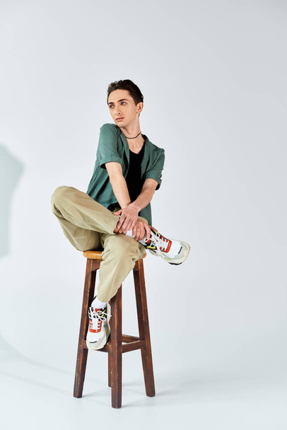 Un giovane omosessuale seduto elegantemente su uno sgabello in uno studio, mostrando fiducia e orgoglio. - Foto, immagini