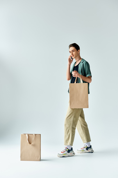 Uma pessoa queer elegante se encaixa confiantemente com sacos de compras contra um fundo branco. - Foto, Imagem