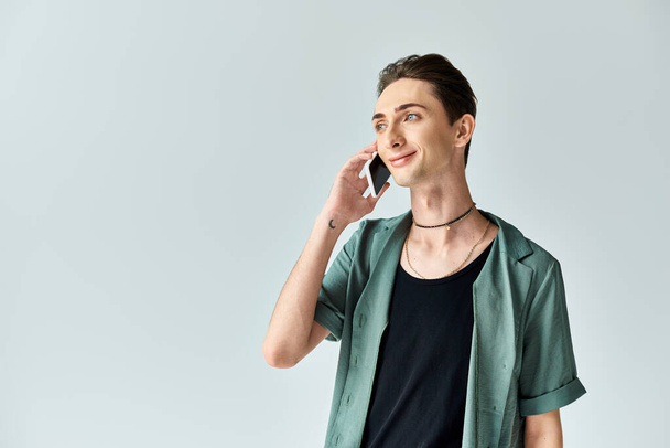 Ein junger queerer Mensch, tief verstrickt in ein Telefonat vor einem heiteren grauen Hintergrund. - Foto, Bild