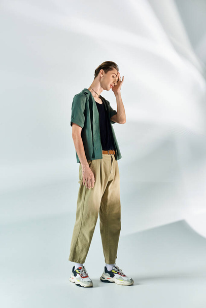Een jonge homo in een bruin hemd en een kaki broek staat vol vertrouwen tegen een effen witte achtergrond. - Foto, afbeelding