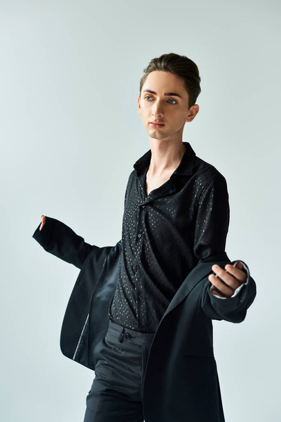 Een jonge homo poseert vol vertrouwen in een studio met een zwart jasje en shirt aan, symbool voor kracht en trots.. - Foto, afbeelding