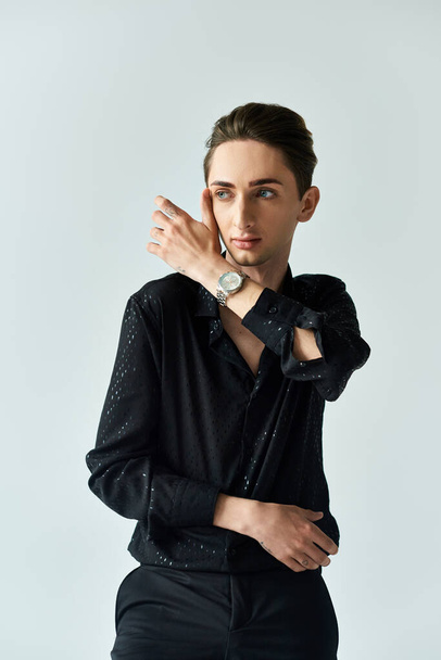 A young man in a black shirt exudes confidence while posing in a studio setting against a grey background, embracing his LGBT identity. - Photo, Image