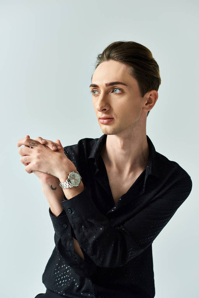 A young man in a black shirt confidently displays his queer pride as he strikes a pose in a studio against a grey background. - Photo, Image