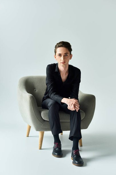 Młody pedał pewnie siedzi na szarym krześle w studio, emanując dumą i pewnością siebie. - Zdjęcie, obraz