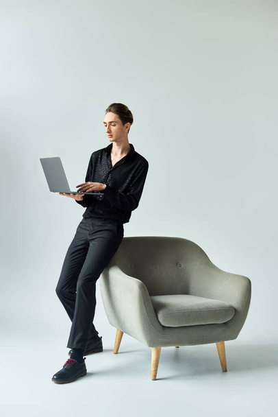 Mladý teplouš sedí na židli s laptopem, vyjadřuje kreativitu a inspiraci, obklopen moderní atmosférou. - Fotografie, Obrázek