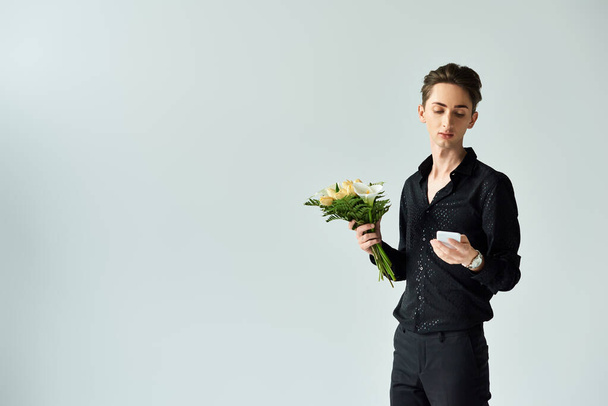 Una giovane persona queer che tiene un mazzo di fiori in uno studio ambientato su uno sfondo grigio. - Foto, immagini