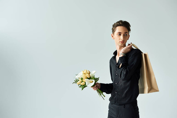 Ένας νεαρός queer άνθρωπος με αυτοπεποίθηση θέτει κρατώντας μια τσάντα αγορών γεμάτη με λουλούδια, εκφράζοντας υπερηφάνεια και χαρά. - Φωτογραφία, εικόνα