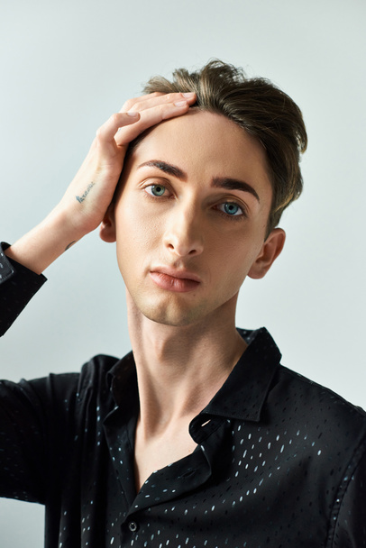 A young queer person strikes a thoughtful pose with his hands resting on his head in a studio setting against a grey background. - Photo, Image