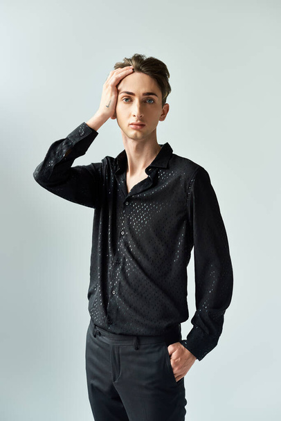 A young queer person in a black shirt and pants strikes a pose against a grey backdrop in a studio setting. - Photo, Image