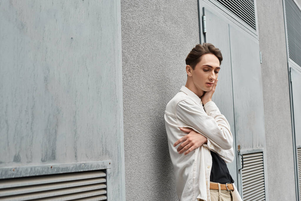 Un jeune homme élégamment habillé s'appuie contre un mur perdu dans ses pensées, exsudant un puissant sens de la contemplation. - Photo, image