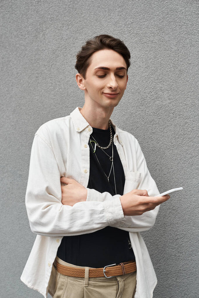 Молода людина в стильному вбранні, що представляє ЛГБТ гордість, тримає мобільний телефон. - Фото, зображення