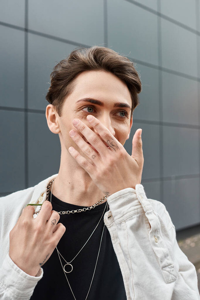 Ένα νεαρό άτομο, μέλος της ΛΟΑΤΚΙ κοινότητας, καλύπτει το πρόσωπό του με τα χέρια του σε μια χειρονομία απόκρυψης.. - Φωτογραφία, εικόνα
