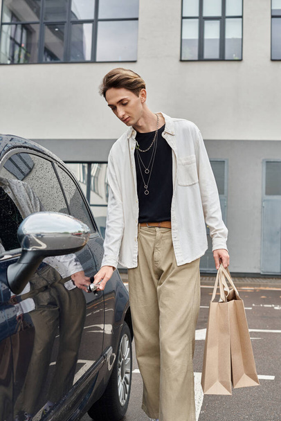 Junge queere Person in stylischer Kleidung beim Entladen von Einkaufstüten aus einem am Straßenrand geparkten Auto. - Foto, Bild