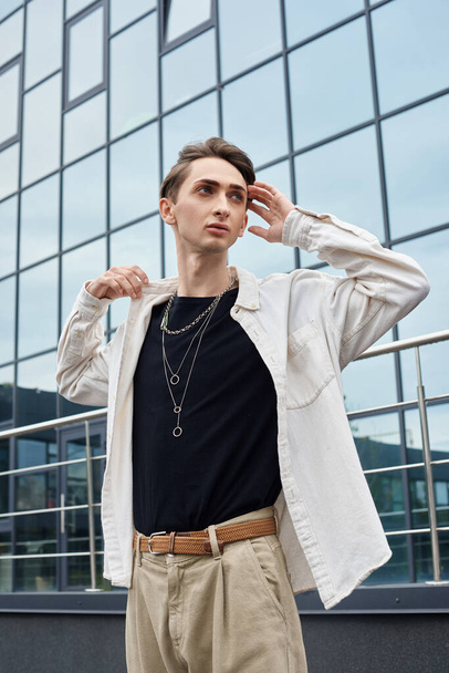 Ένας νεαρός queer άνθρωπος αποπνέει εμπιστοσύνη σε ένα κομψό λευκό πουκάμισο και χακί παντελόνι, ενσωματώνοντας υπερηφάνεια και αυτο-έκφραση. - Φωτογραφία, εικόνα