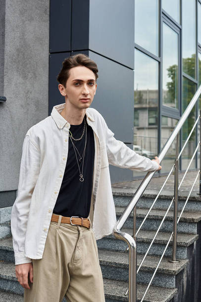 Um jovem indivíduo transpira confiança em uma camisa branca e calças cáqui, mostrando sua identidade gay com orgulho e estilo. - Foto, Imagem