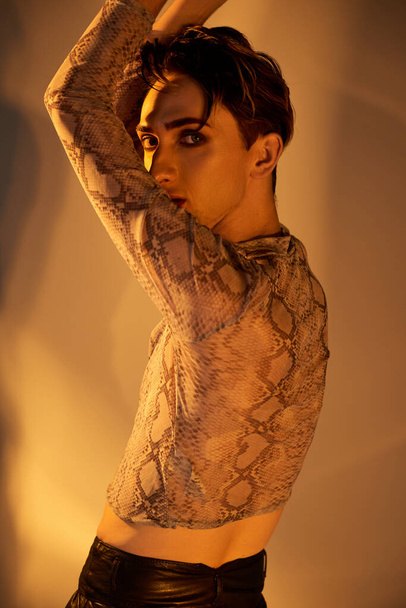 Una joven queer en una llamativa parte superior de piel de serpiente posa frente a un espejo, exudando confianza y estilo. - Foto, imagen