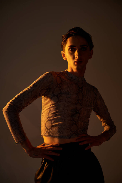 Uma jovem queer faz uma pose elegante na frente de um fundo escuro, exalando confiança e orgulho. - Foto, Imagem