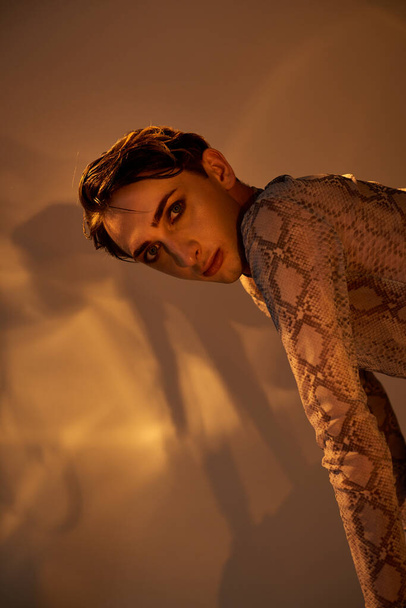 Uma jovem queer pessoa em um vestido de pele de cobra encostada a uma parede, exalando estilo e confiança. - Foto, Imagem