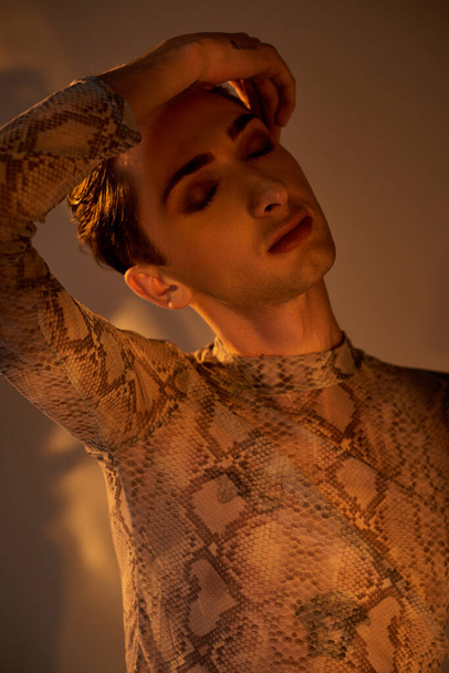Jeune homme queer posant avec confiance dans une chemise élégante en peau de serpent, exprimant la fierté LGBT. - Photo, image