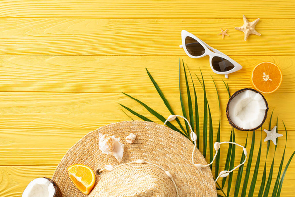 Zomer paradijs gevangen: bovenaanzicht strohoed, zonnebril, vers exotisch fruit - sinaasappels, kokosnoten, palmblad, schelpen, en zeesterren op een zonnig geel bureau - Foto, afbeelding