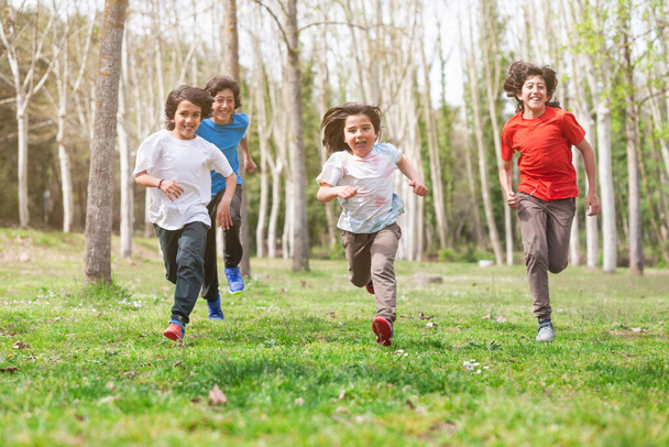 Hermanos de diferentes edades corriendo hacia la cámara a través de un prado con árboles. El más joven está al frente..  - Foto, imagen