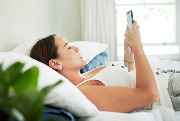 Женщина, дома и лежит в постели со смартфоном на перерыве для социальных сетей, смс и общения. Женщина, спальня и мобильный телефон в отпуске или выходной день, чтобы расслабиться, расслабиться и успокоиться с онлайн знакомств. - Фото, изображение
