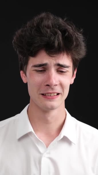Szomorú és melankolikus fehér fiatalember sír és sír a fekete háttér miatt. Érzelmi stressz és magány koncepció. Függőleges videó. - Felvétel, videó