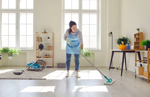 Young maid the mopping floor with a mop at home. This scene captures the essence of household service and the dedication of a modern maid tending to the cleaning of the living space. - Foto, imagen