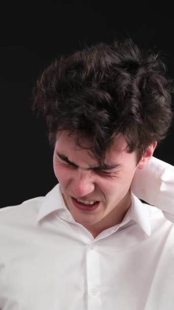Boldogtalan kaukázusi fiatalember szenved fejfájás vagy migrénes fájdalom, álló fekete alapon. Rossz egészségi állapot. Függőleges videó. - Felvétel, videó