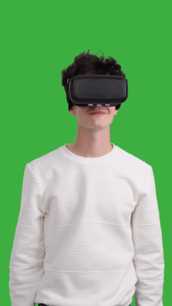 Joven caucásico feliz y alegre usando auriculares VR sobre fondo de croma key. Tecnología de innovación, entretenimiento futurista. Vídeo vertical. - Imágenes, Vídeo