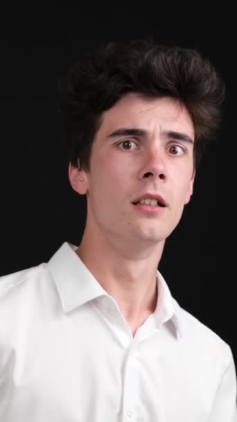 Portrait of a scared and frustrated Caucasian young man is frightened on black background. Panic, stress, nightmare concept. Vertical video. - Footage, Video