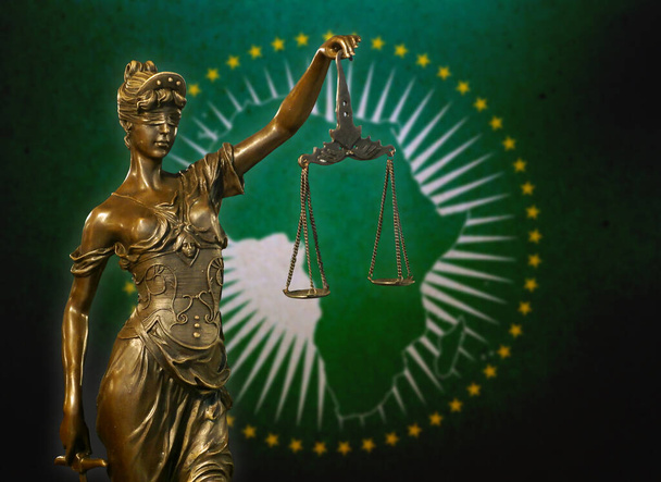 Close-up van een klein bronzen beeldje van Lady Justice voor een vlag van de Afrikaanse Unie. - Foto, afbeelding